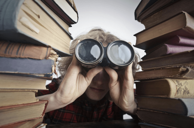 Discovery: A person looking through a stack of books with a pair of binoculars.